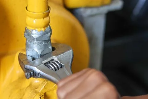 Worker using an adjustable wrench on a yellow industrial pipe. Stock Photos
