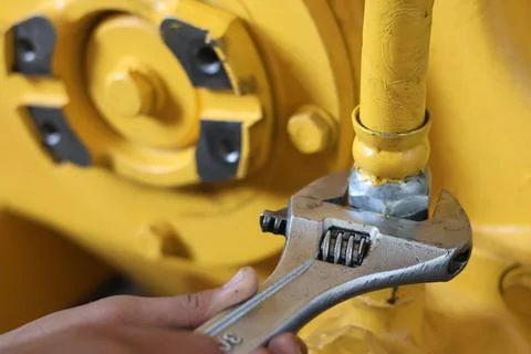 Worker using an adjustable wrench on a yellow industrial pipe. Stock Photos