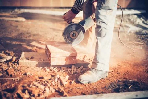 Worker using an angle grinder on construction site for cutting bricks, debris Stock Photos