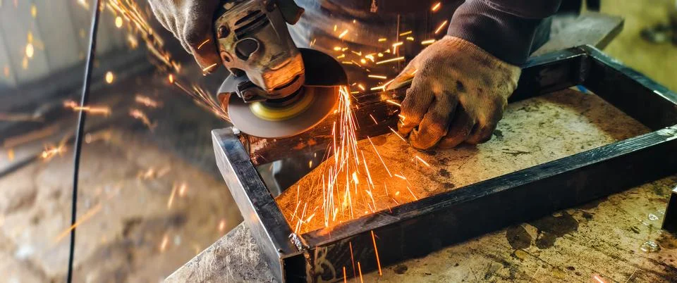 Worker using an angle grinder to cut and shape metal, producing a shower of Stock-Fotos