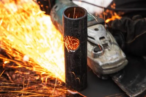 Worker using an angle grinder to cut a steel pipe, sending bright orange spar Stock Photos