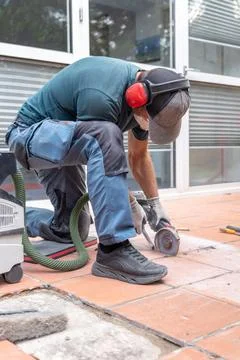 Worker using angle grinder to cut terracotta floor tiles outdoors Photos