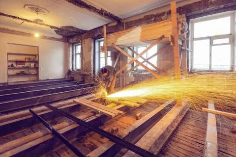 Worker is using angle grinder with fountain of sparks in apartment that is under Stock Photos