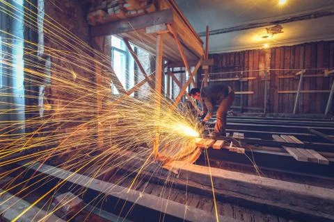 Worker is using angle grinder with fountain of sparks in apartment that is under Stock Photos