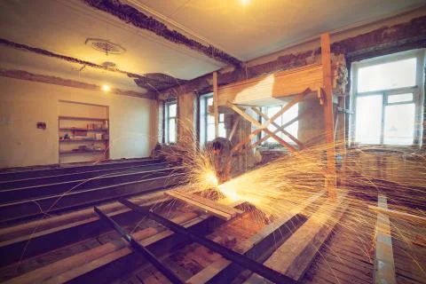 Worker is using angle grinder with fountain of sparks in apartment that is under Stock Photos