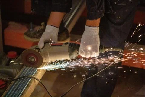 Worker is using angle grinder with fountain of sparks in apartment that is under Stock Photos