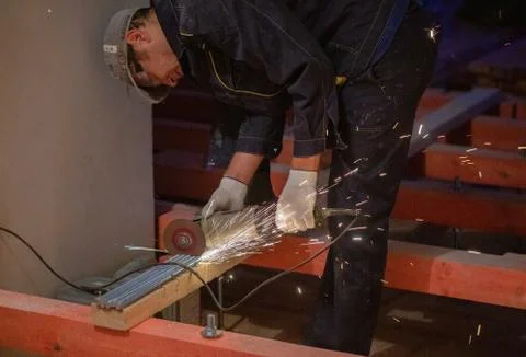 Worker is using angle grinder with fountain of sparks in apartment that is under Stock Photos