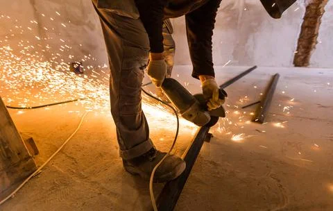 Worker is using angle grinder with fountain of sparks in apartment that is under Stock Photos