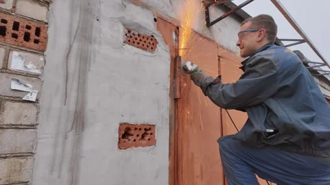 Worker using angle grinder on metal garage door 스톡 동영상 335283676