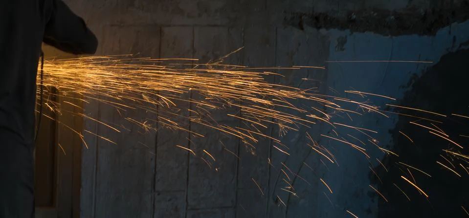 A worker using angle grinder in a workshop with sharp orange sparks Stock Photos
