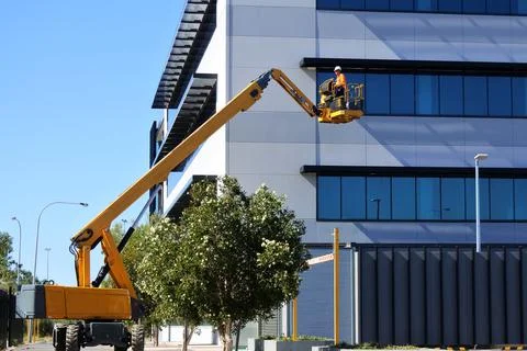 Worker using an  articulated boom lift beside a building exterior Stock Photos