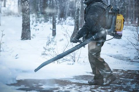 A worker is using a backpack blower to clear snow on a cold winter day in t.. Stock Photos