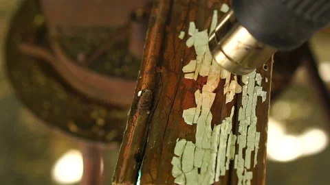 Worker using a building hair dryer heats paint on a wooden bar and cleans it wit Stock Footage 116017777