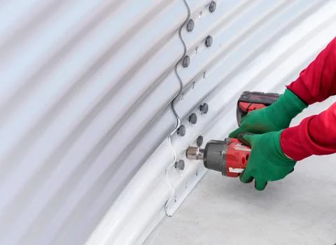 The worker is using a cordless impact wrench to tighten bolts on the metal .. Stock Photos