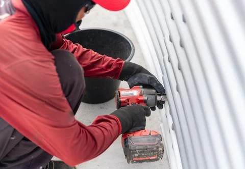 The worker is using a cordless impact wrench to tighten bolts on the metal .. Stock Photos