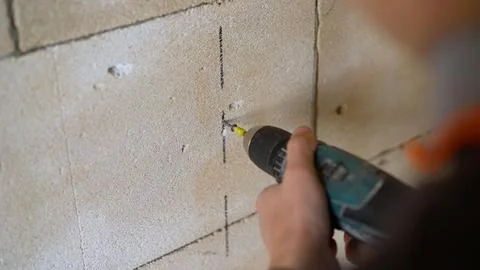 Worker using a cordless power drill to make a hole in a block wall. Stock-Fotos