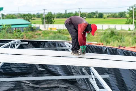 A worker is using a cordless screwdriver to remove screws from the metal sh.. Stock Photos