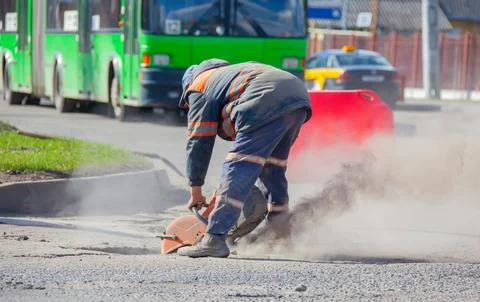 A worker is using a cutting tool to remove asphalt on the road while traffic Foto stock