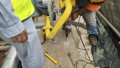 Worker using a drill on a construction site with tools and machinery in view. Photos