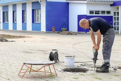 Worker using a drill to perform maintenance next to an open manhole, safety Stock-Fotos