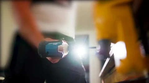 Worker using drill on workbench with light in background, slow motion moody Stock Footage 193985669