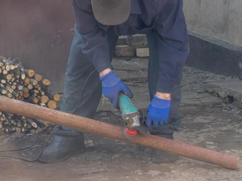 Worker using an electric angle grinder to clean rust from a metal pipe at a.. Stock Photos