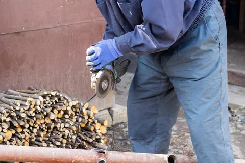 Worker using an electric angle grinder to cut metal pipe outdoors, emphasiz.. Stock Photos