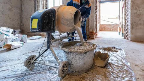 Worker is using the electric concrete mixer in an apartment is under Stock Photos
