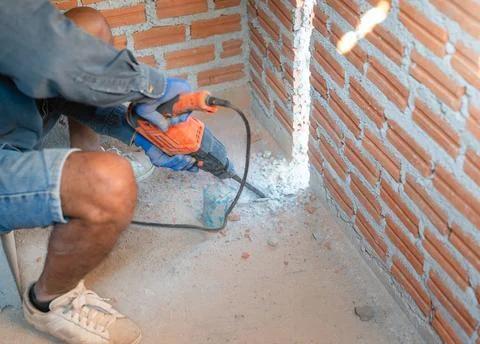 Worker using an electric demolition hammer to break a concrete floor near a.. Stock Photos