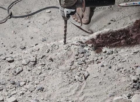 Worker Using Electric Drill on Concrete Surface During Construction Stock Photos