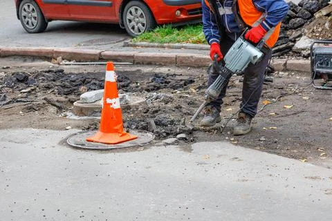 A worker using an electric jackhammer and a gasoline generator cleans the are Stock Photos