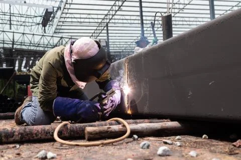 Worker using electric wheel grinding on steel structure in factory. Stock Photos