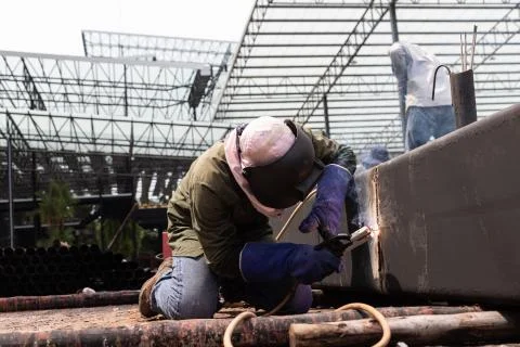 Worker using electric wheel grinding on steel structure in factory. Stock Photos