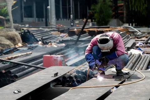 Worker using electric wheel grinding on steel structure in factory. Stock Photos