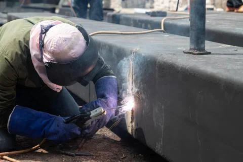 Worker using electric wheel grinding on steel structure in factory. Stock Photos
