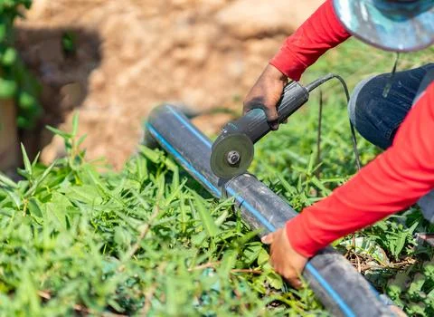 A worker using a handheld angle grinder to cut a black HDPE pipe outdoors o.. Stock Photos