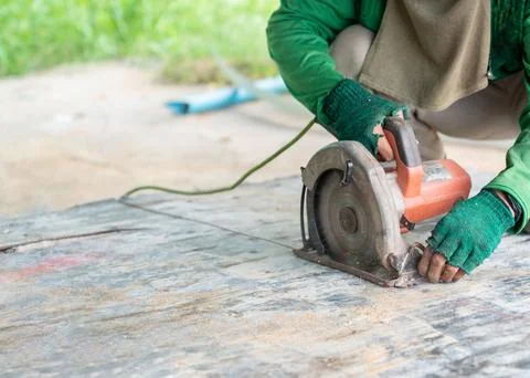 Worker using a handheld circular saw to cut wooden board outdoors. Stock-Fotos