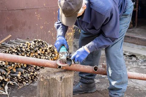 Worker using a handheld electric grinder to cut a rusted metal pipe outdoor.. Stock Photos