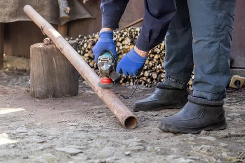 Worker using a handheld power grinder to smooth a rusty metal pipe outdoors.. Stock Photos