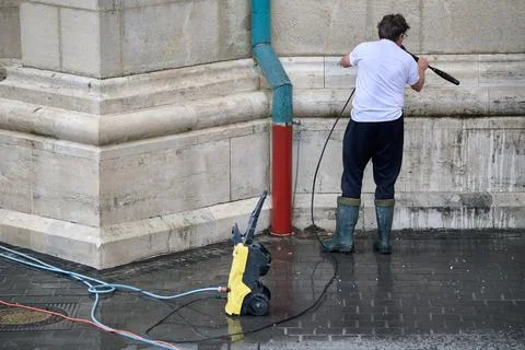 Worker using a high-pressure water washer to clean the exterior stone wall an Stock Photos