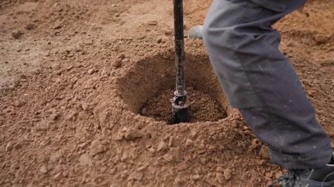 Worker using manual digging tool beside freshly cut hole in dry soil, with low Video stock 347691996