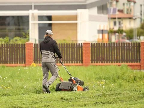 Worker using a manual lawn mower mows grass on near the house. Landscaping .. Stock Photos