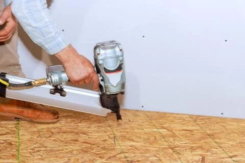 Worker using a nail gun to install plywood flooring in a construction setting Stock Photos