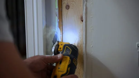 Worker using an oscillating power tool to cut drywall and wood around a door 스톡 동영상 347574418