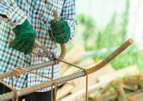 A worker is using pliers to tie wire around rebar at the construction site. Stock-Fotos