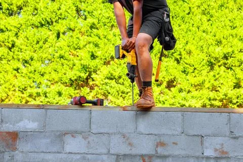 Worker using power drill on concrete wall during construction Stock Photos