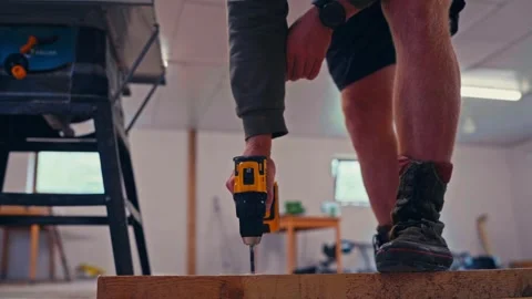 A Worker is Using a Power Drill to Screw Into a Wooden Board Inside a Workshop Stock Footage 335291335