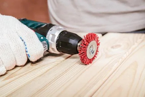 Worker Using Power Drill With Wire Brush On Wooden Plank Foto stock