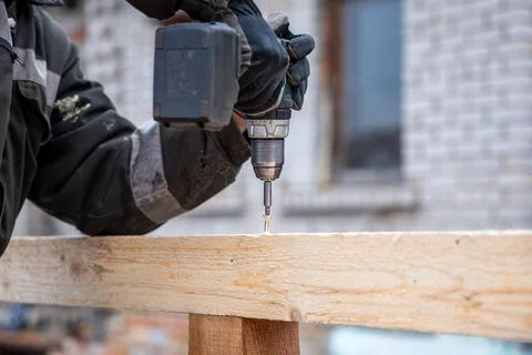 Worker Using Power Drill on Wooden Beam with Brick Building Background Stock Photos