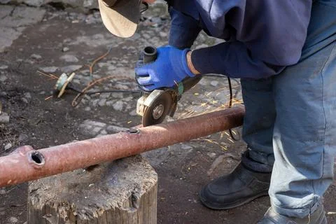 Worker using a power grinder to cut a rusty metal pipe on a wooden stump, i.. Stock Photos